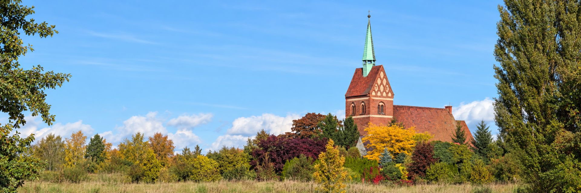 Kościół Narodzenia NMP w Wilkowie wśród jesiennych drzew, pod błękitnym niebem